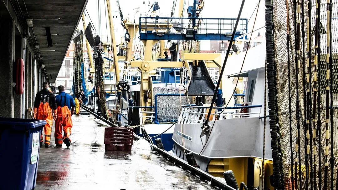 A fishing vessel moored at a quay, crew in orange oilskins on deck